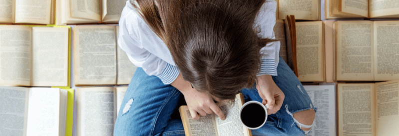 Foto desde arriba de una chica leyendo y tomando el café