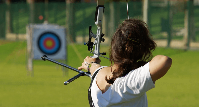 Foto de una chica tirando con arco una flecha a una diana de fondo